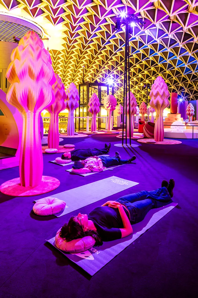 Visitors lying on mats under pink and purple light in Next Nature Museum